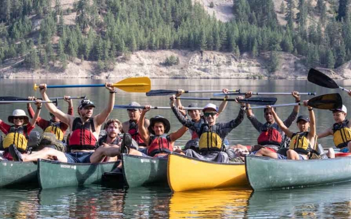 a group of boys sitting in canoes raise their paddles in the air in celebration on an outward bound course